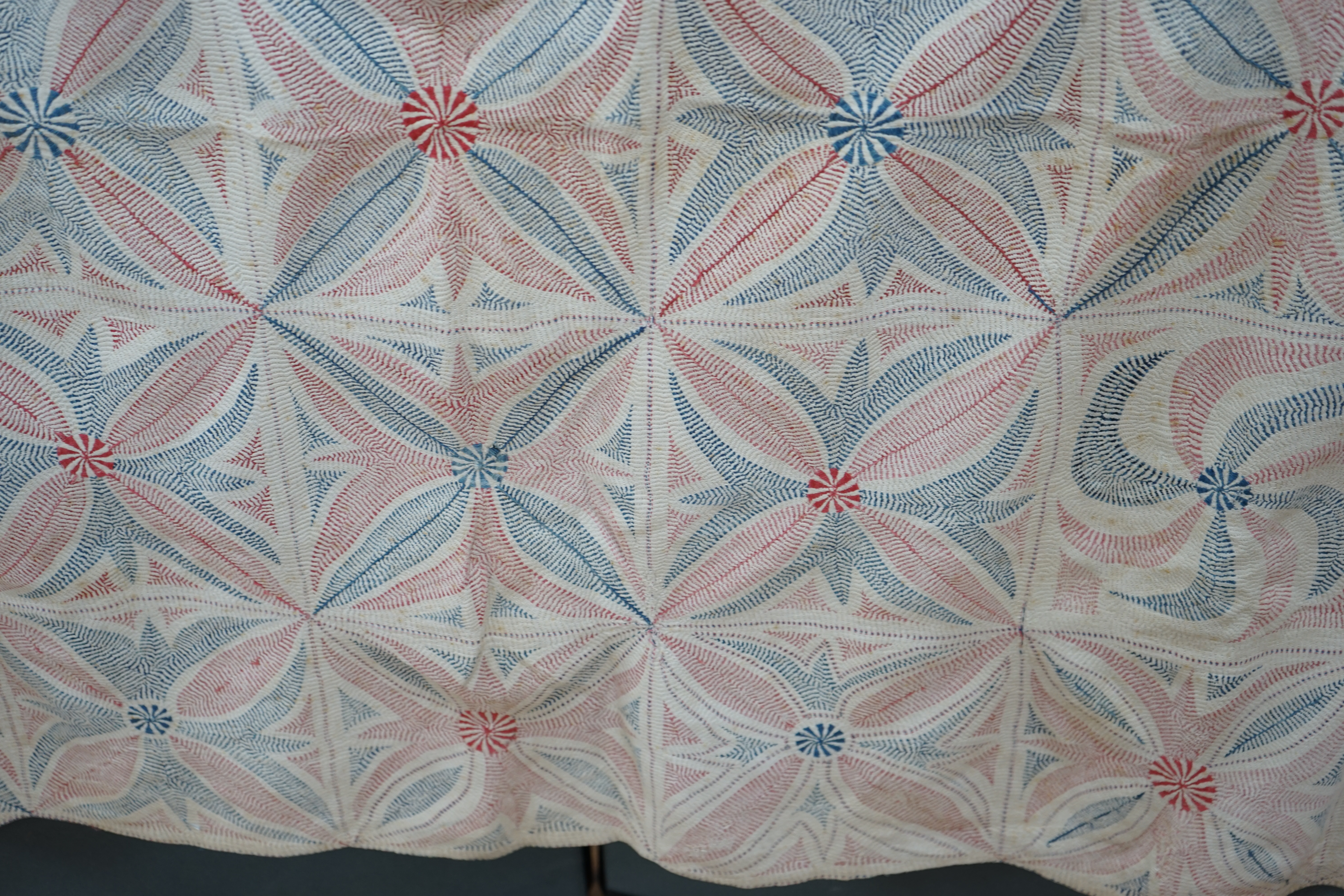 An early 20th century West Bengal Kantha embroidered quilt, embroidered on cream cloth (possibly made from layers of old saris) embroidered in blue and red threads, designed in squares of large abstracted floral motifs u